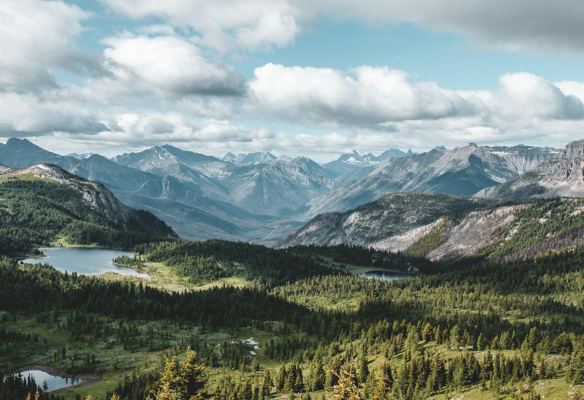 Panoramic view from a mountain, featuring serene lakes surrounded by majestic mountains under a clear sky.
